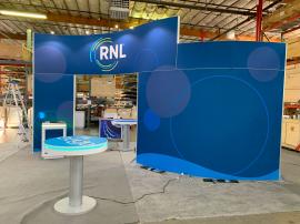 RENTAL: RE-9135 Island Rental Design with 16’ High Curved Gravitee Panel System Structure with (1) RE-1576 White Laminated Reception Counter, (2) RE-1575 White Laminated Workstation Counters, (4) Large Monitor Mounts, (8) LED Arm Lights, SEG Fabric Grap